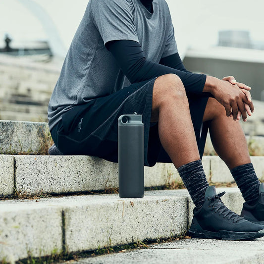 Person sitting on steps with a water bottle next to them, wearing athletic gear.