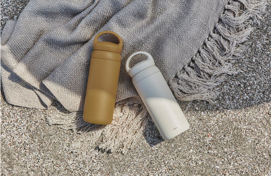 Two insulated bottles, one brown and one white, on a textured fabric surface.