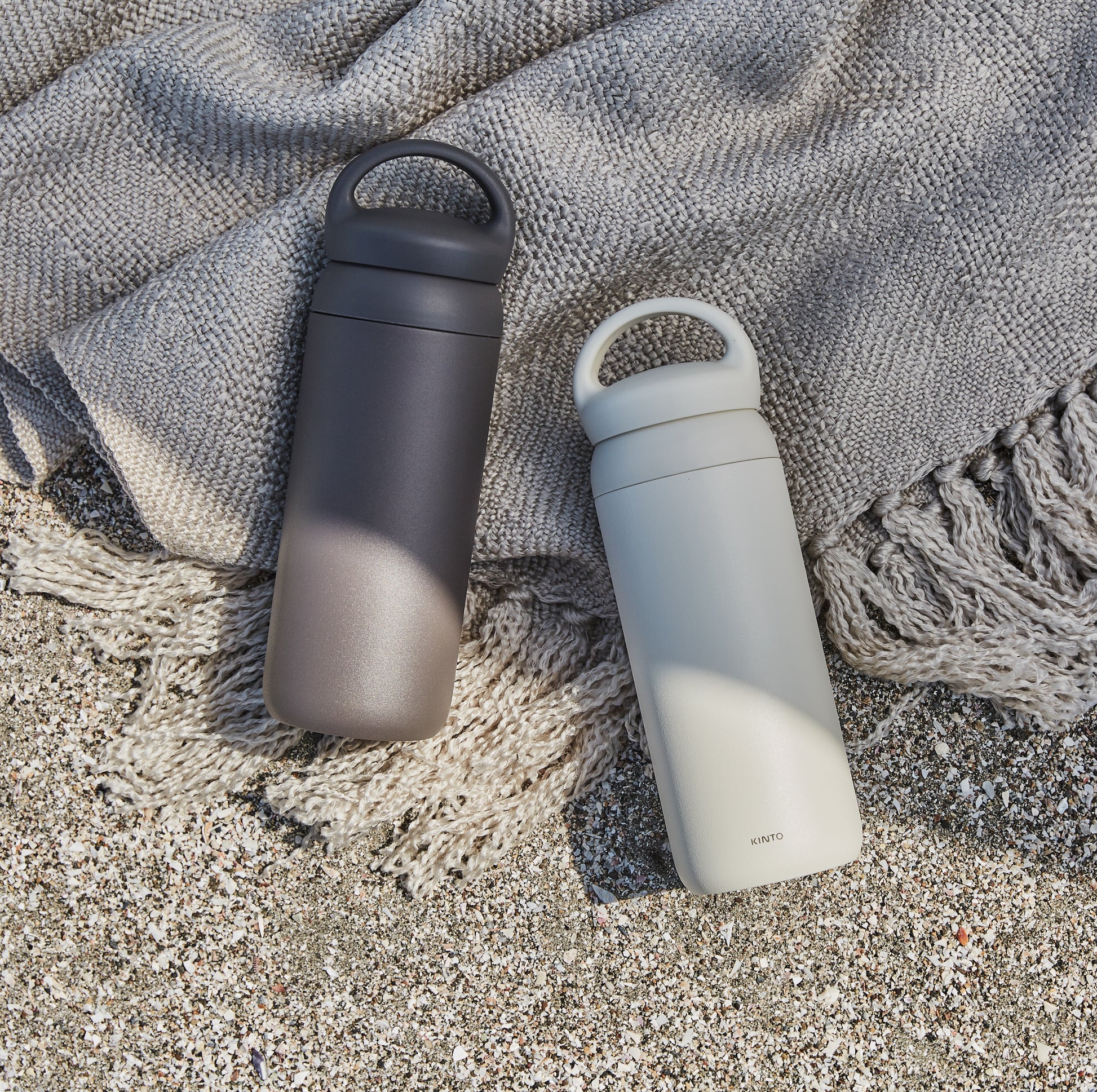 Two insulated bottles on a textured blanket with sand underneath