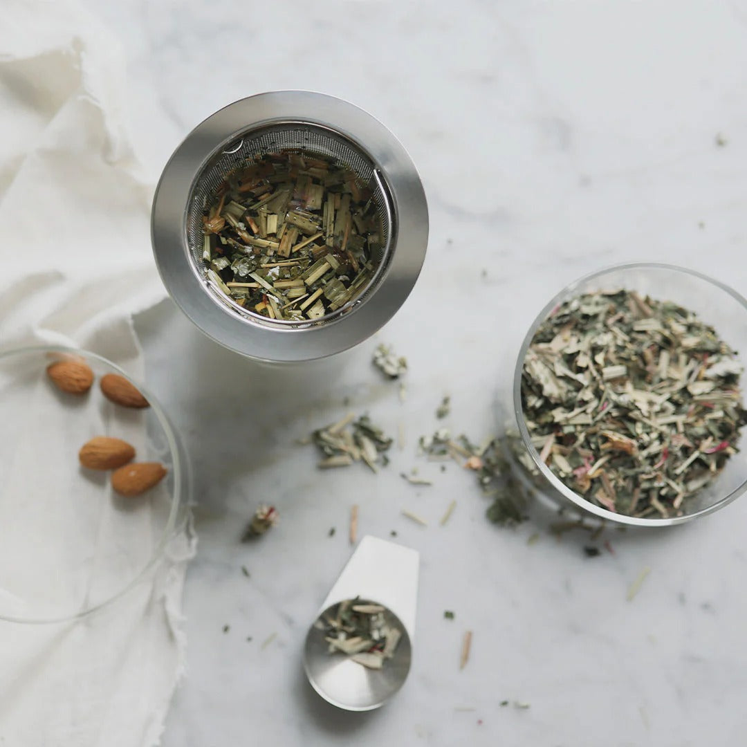 Herbal tea mix in a glass container with a spoon on a marble surface