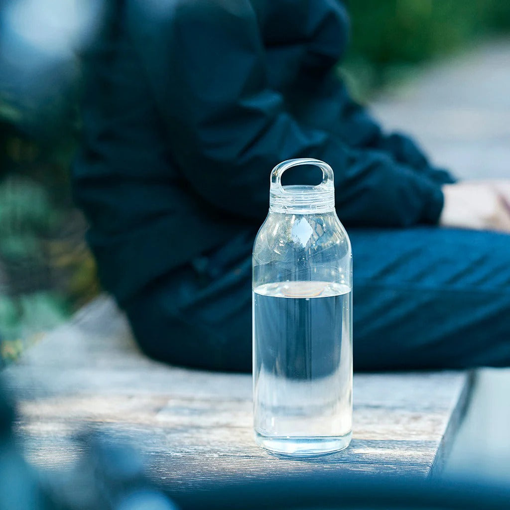 Clear water bottle on a wooden surface with a blurred person in the background