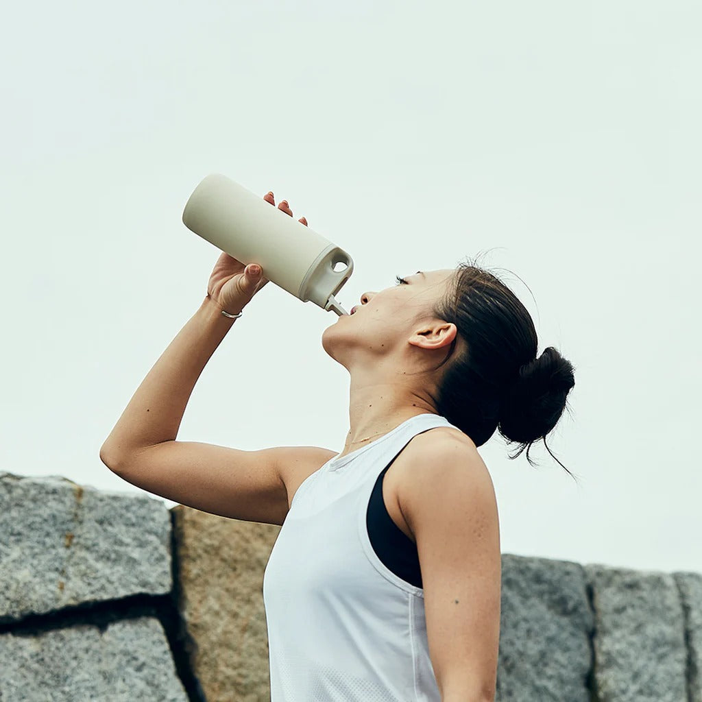 Woman drinking from a water bottle against a light background