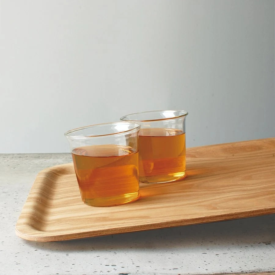 Two glasses of amber liquid on a wooden tray with a plain background