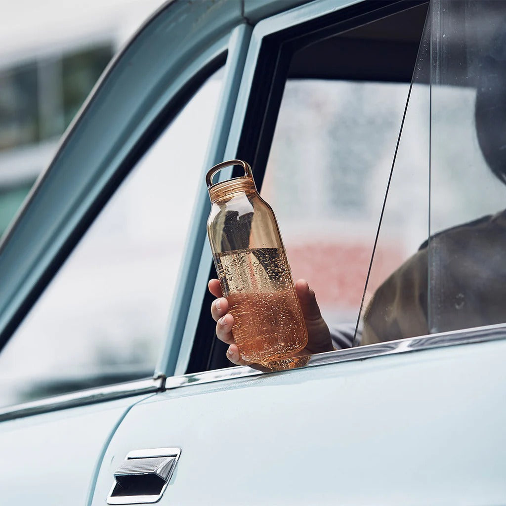 Person holding a clear bottle with a car window open, possibly to let in fresh air or ventilation.