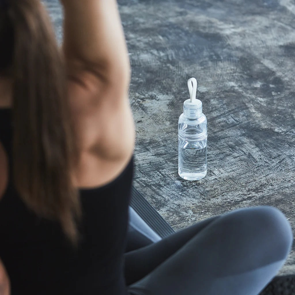 Person sitting on a yoga mat with a clear water bottle nearby