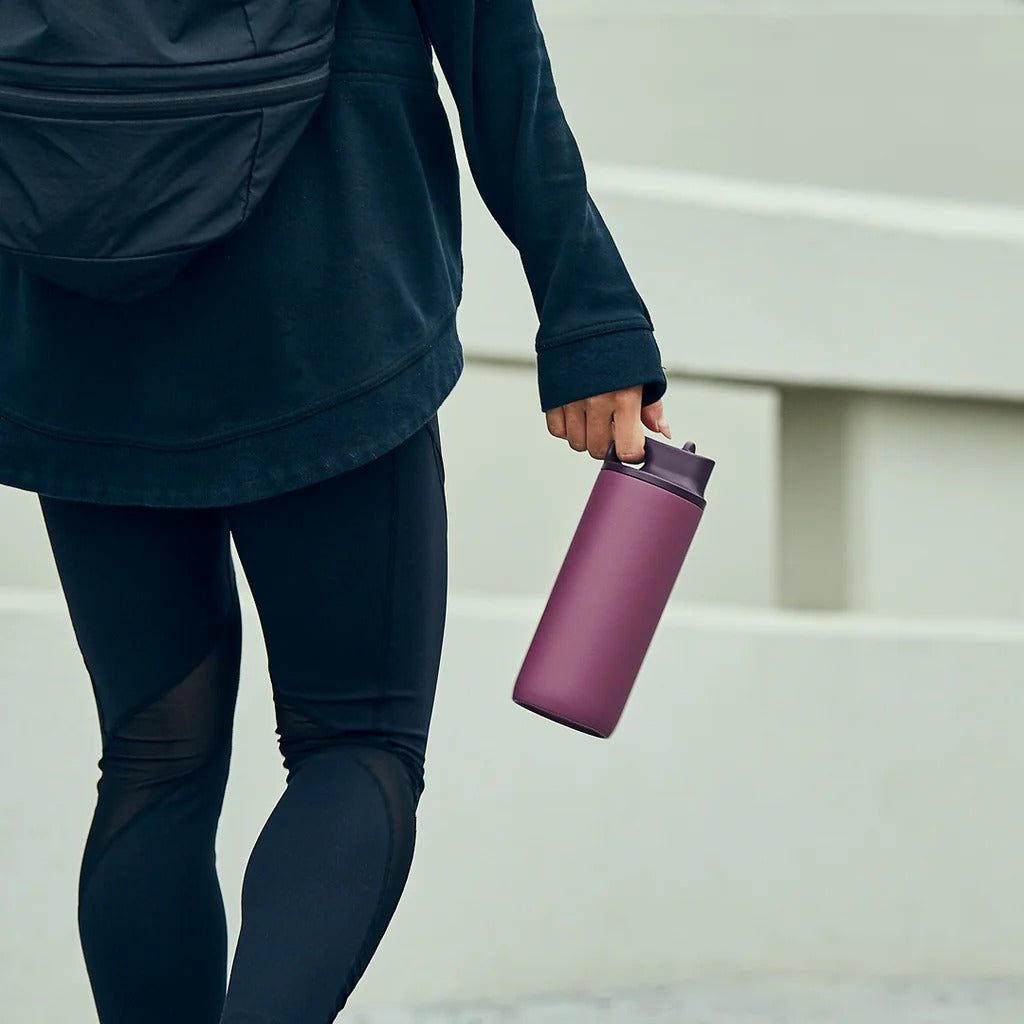 Person in dark athletic wear holding a purple water bottle on steps