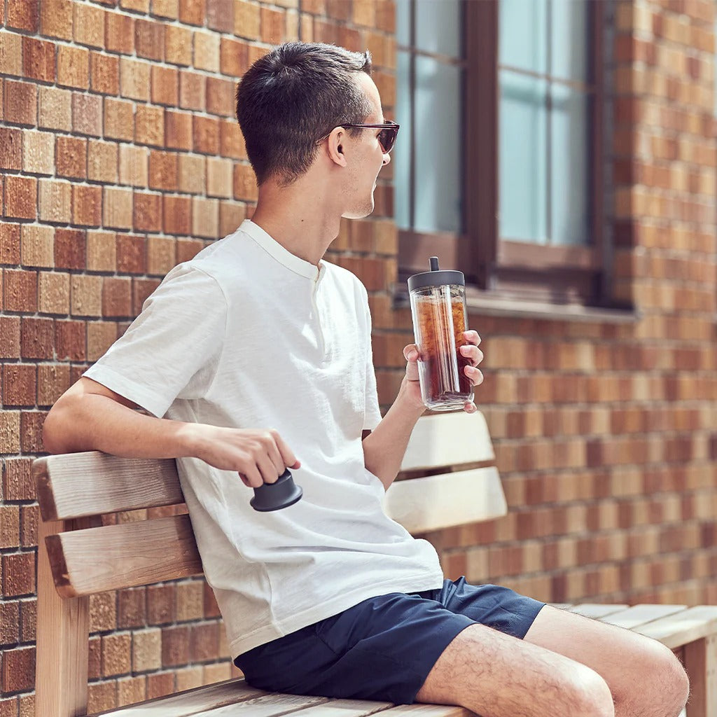 Man sitting on a bench holding a coffee cup against a brick wall.