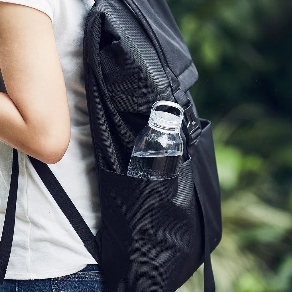 Person with a black backpack holding a clear water bottle outdoors