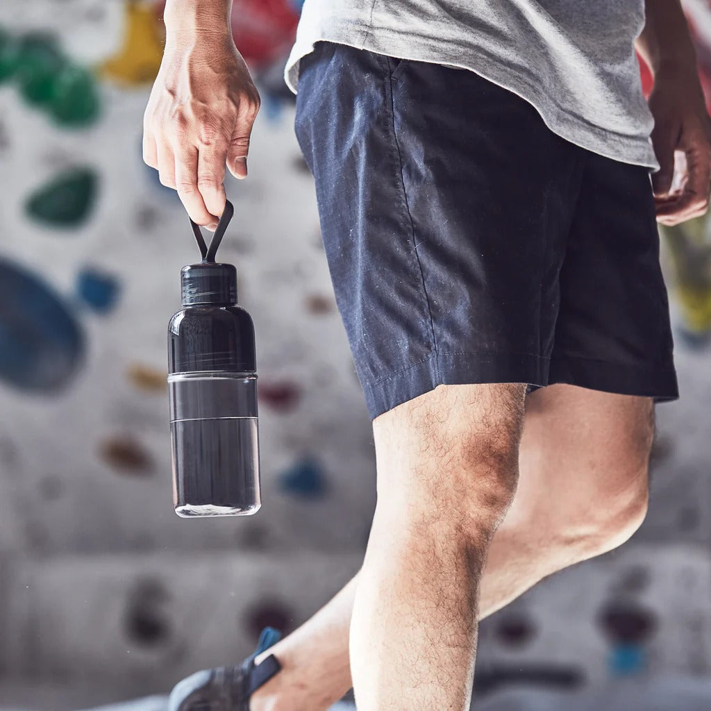 Person holding a black water bottle with a climbing wall in the background