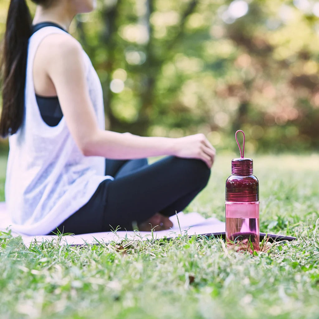 Person sitting on grass with a pink water bottle nearby