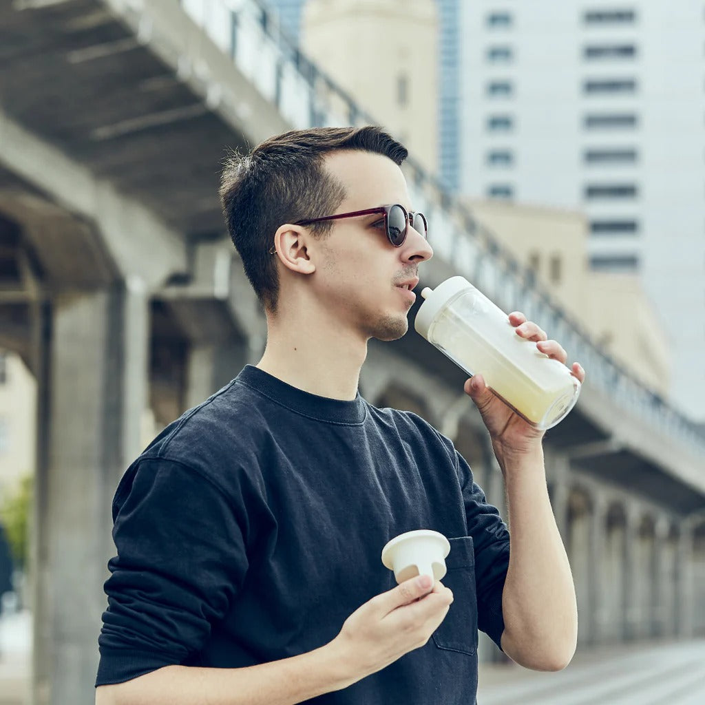 Man drinking from a reusable water bottle outdoors with a blurred background