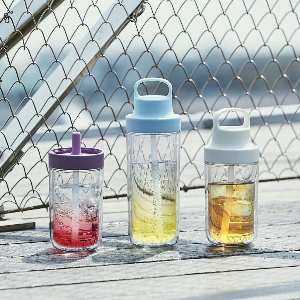 Three water bottles with different colored lids on a wooden surface with a chain-link fence in the background.